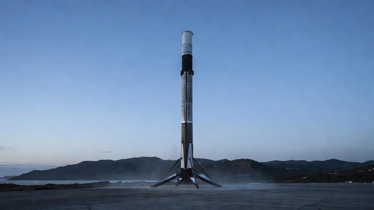 A Falcon 9 first-stage booster stands upright on a concrete landing pad with its legs deployed.