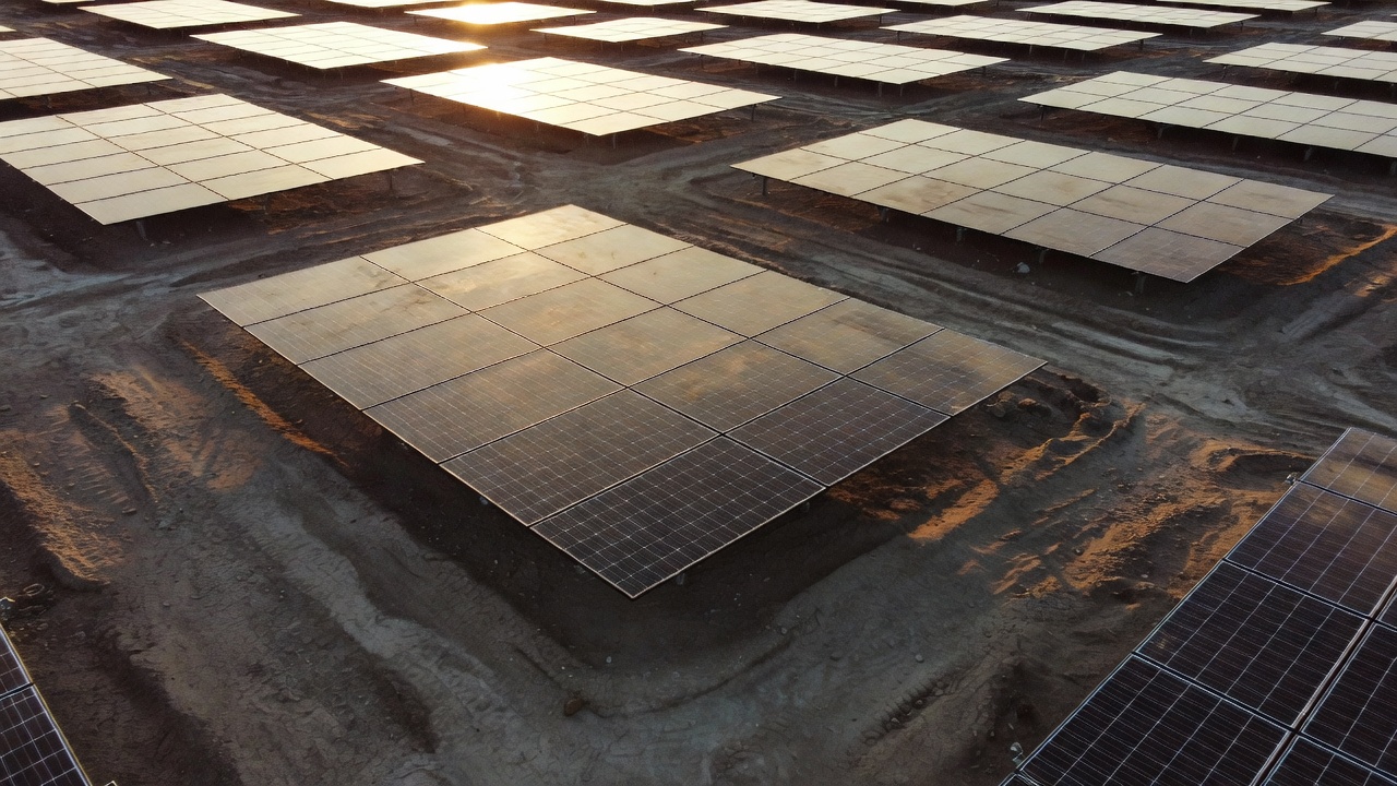Aerial macro on the Northeast plant's Erthos array shows panels bolted directly to bare graded earth, no steel racking beneath, warm low-angle sunlight raking across soil-panel contact points.